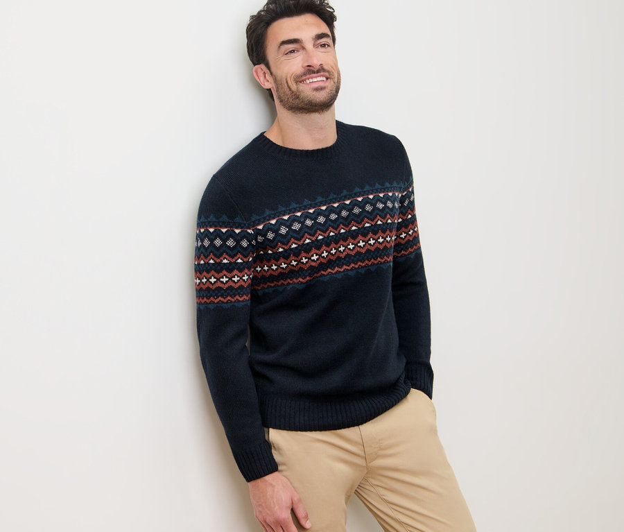 Un homme appuyé contre un mur portant un pull en maille.