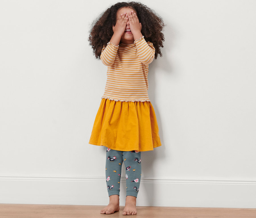 Une fille se couvre les yeux et porte 2 leggings thermiques pour enfant, poule.