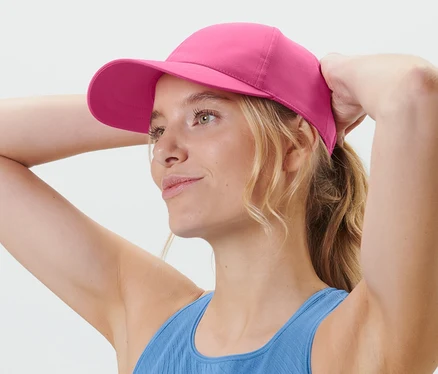 Une femme blonde ajuste sa casquette de sport rose.