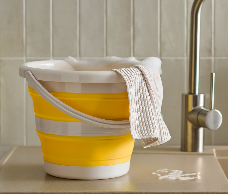 Un seau pliable jaune est posé sur un comptoir avec un chiffon et une bouteille.