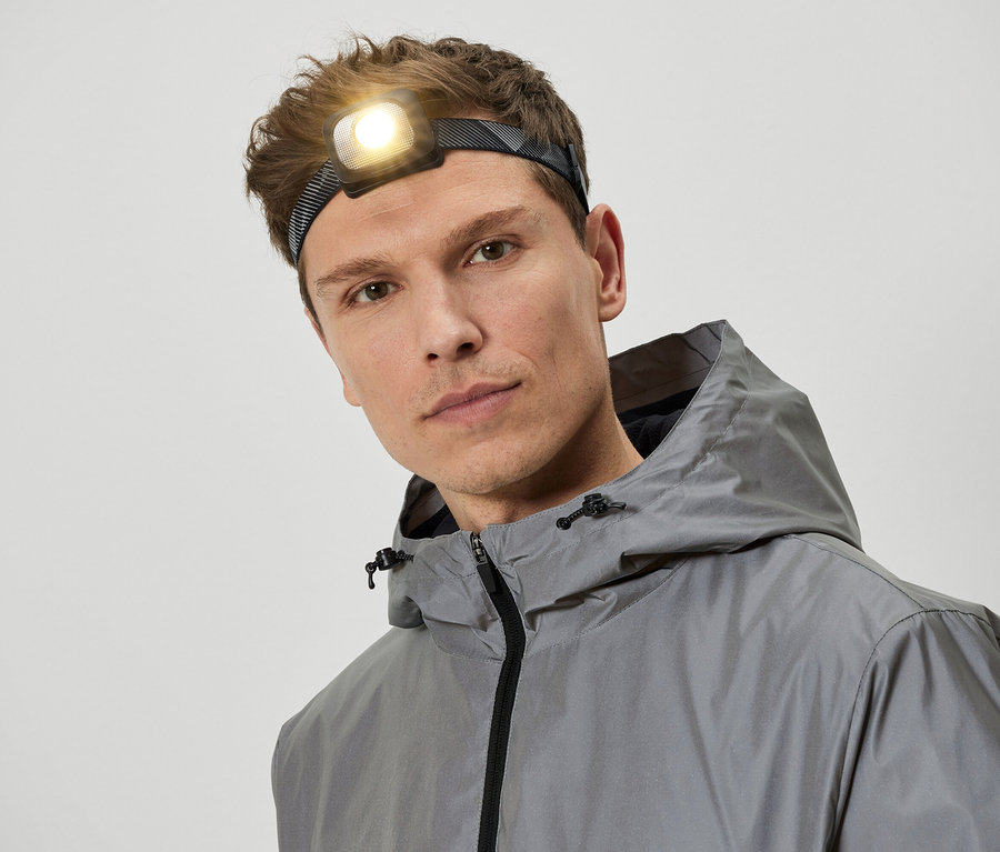 Un homme portant une lampe frontale et une veste à capuche grise.