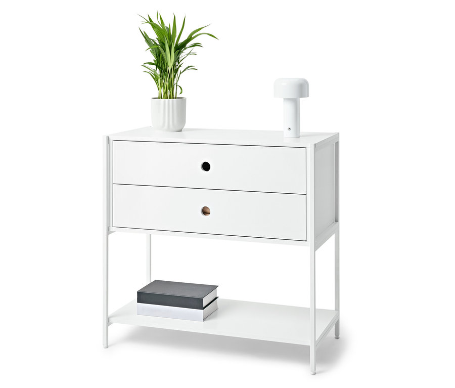 Table de chevet blanche avec deux tiroirs, une lampe, une plante en pot et des livres.