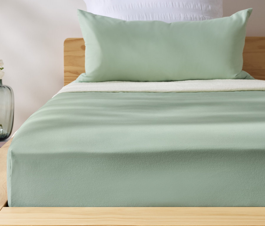 Drap-housse vert en microfibre sur un lit. Un vase avec des fleurs est à côté du lit.