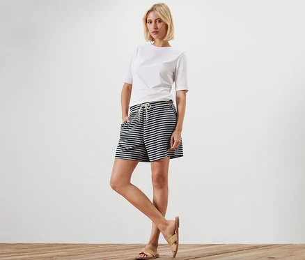 Une femme pose, portant un short rayé en tissu éponge et un t-shirt blanc.