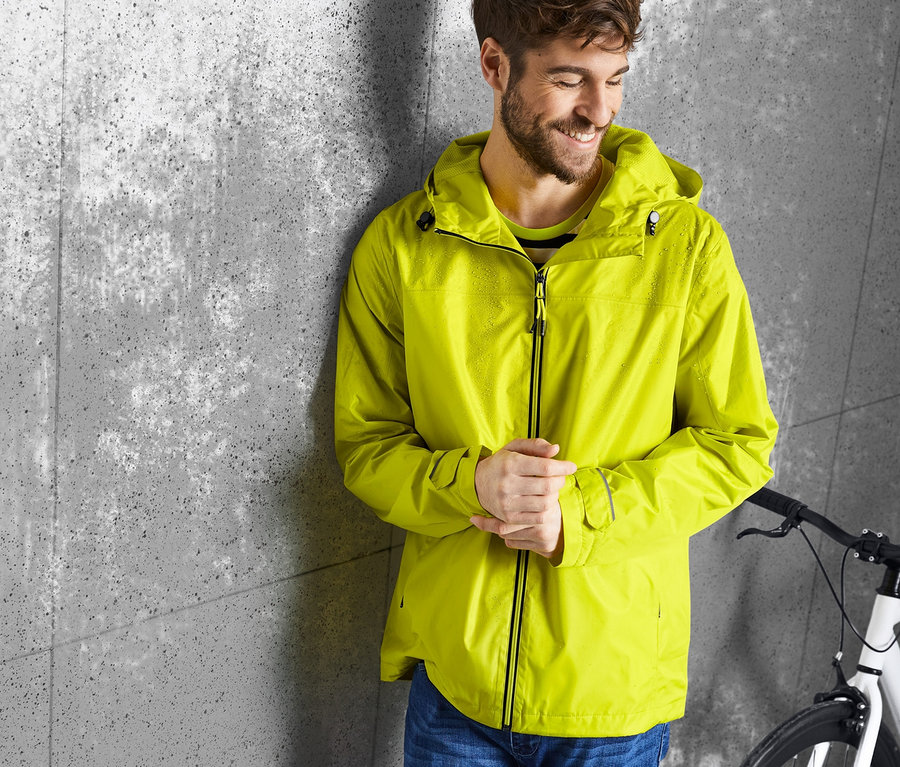 Un homme appuyé contre un mur porte une veste de pluie jaune.