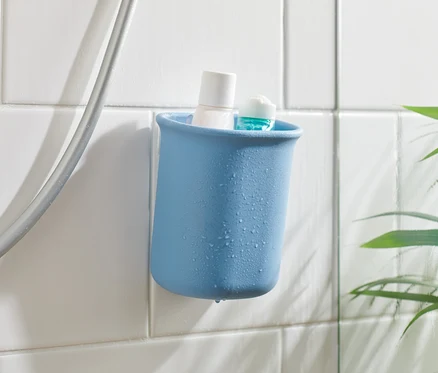 Un organisateur de salle de bain bleu avec un produit blanc et un produit bleu à l'intérieur, fixé sur des carreaux blancs à côté d'un tuyau de douche.