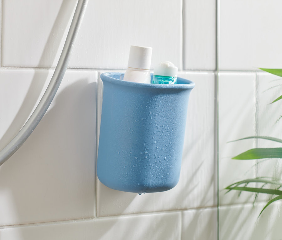 Un organisateur de salle de bain bleu avec un produit blanc et un produit bleu à l'intérieur, fixé sur des carreaux blancs à côté d'un tuyau de douche.