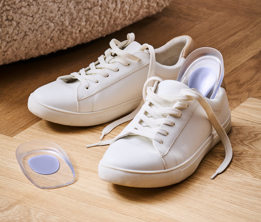 Deux baskets blanches avec des lacets blancs sur un plancher en bois avec une semelle en gel.