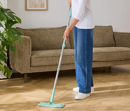 Une femme nettoie un parquet avec une serpillère à base vert turquoise.